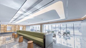 A modern lobby with a green sofa, wooden stools, a reception desk, and large windows offering a view of the street. - Ji Hotel (Taiyuan)