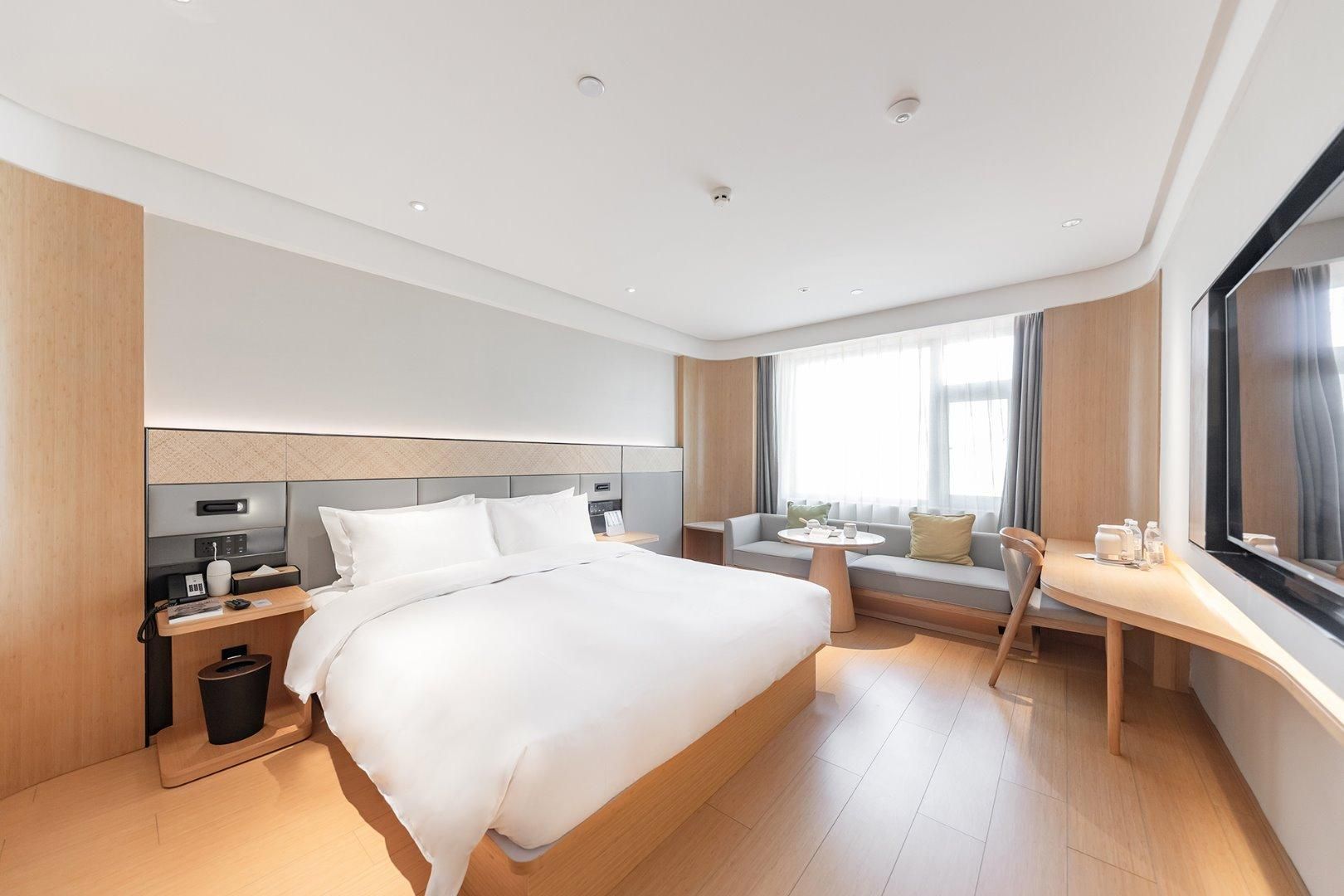 Une chambre d’hôtel moderne dotée d’un grand lit, de tables de chevet, d’un bureau et d’un coin salon offrant une vue sur la ville.