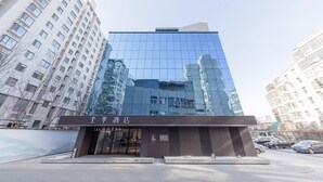 A modern hotel with a glass facade reflecting surrounding buildings, a ground-level entrance, and a visible sign in a foreign language. - Ji Hotel (Taiyuan)