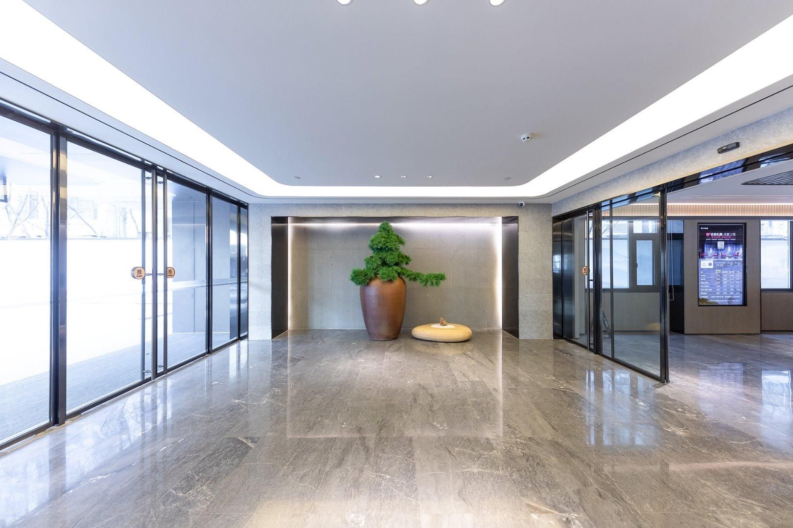 A modern lobby with glass doors, a large planter, and a digital information board.