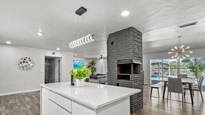 A modern kitchen with a central island, a built-in brick fireplace, and a dining area with a view of the outdoors. - MODERN HOME WITH GYM, SAUNA, POOL AND GAME ROOM (El Paso)