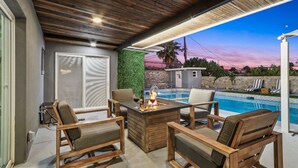 An outdoor seating area with a pool, wooden furniture, and a fire feature. - MODERN HOME WITH GYM, SAUNA, POOL AND GAME ROOM (El Paso)
