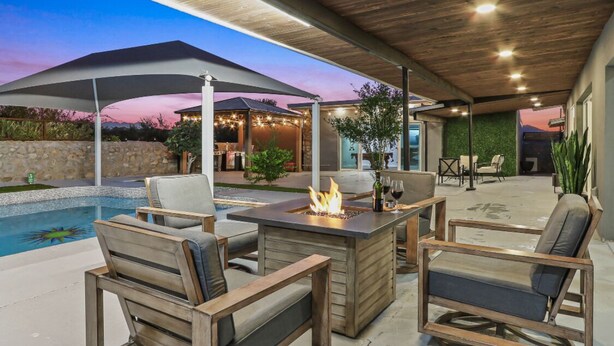 An outdoor patio area with a pool, wooden furniture, and a fire feature. - MODERN HOME WITH GYM, SAUNA, POOL AND GAME ROOM (El Paso)