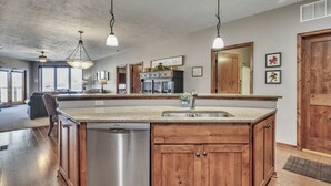 Une cuisine spacieuse dotée d’un grand îlot central, d’un lave-vaisselle en acier inoxydable, de meubles en bois et de luminaires suspendus.