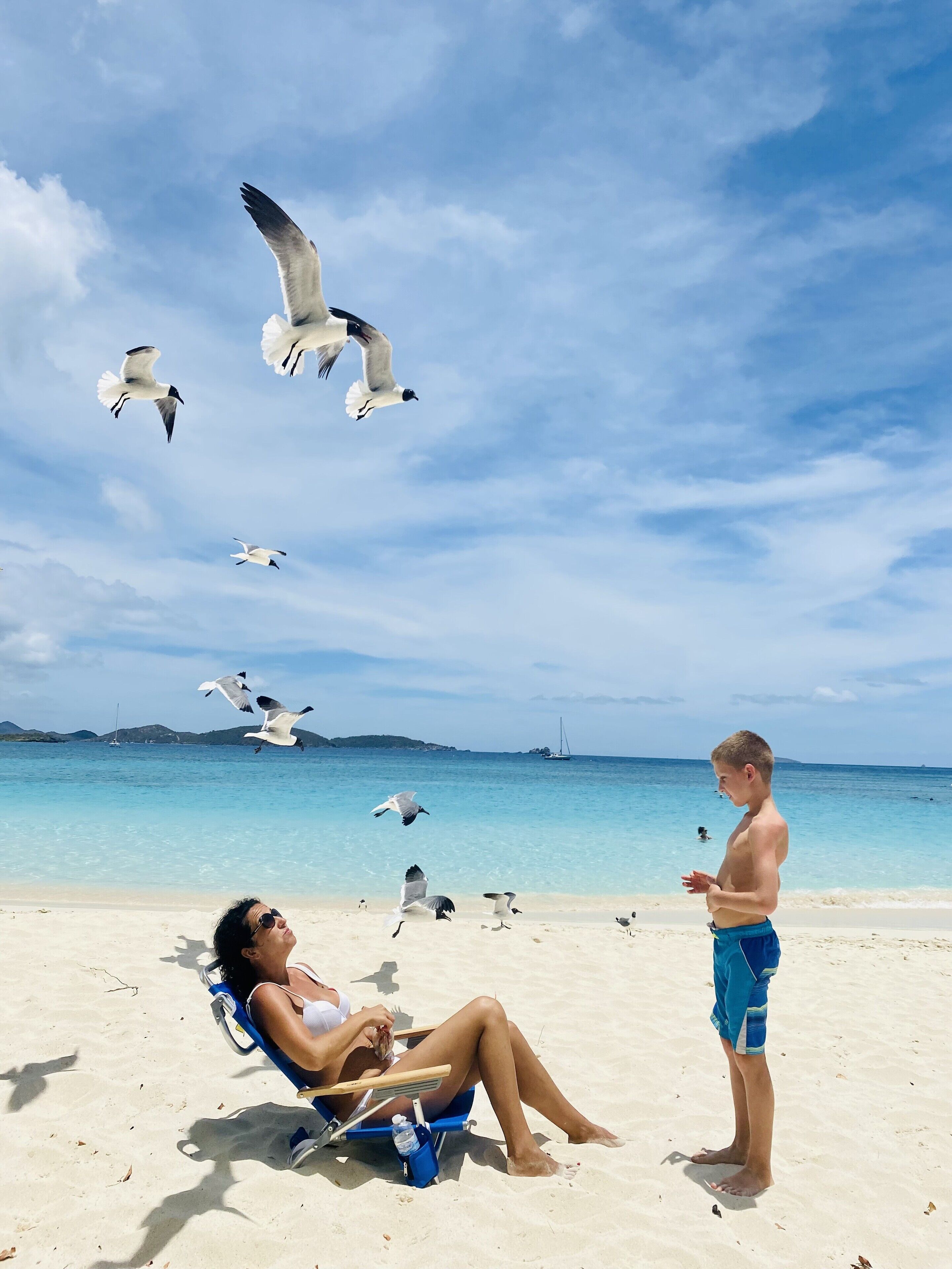 A beach scene with a woman in a chair and a boy standing.