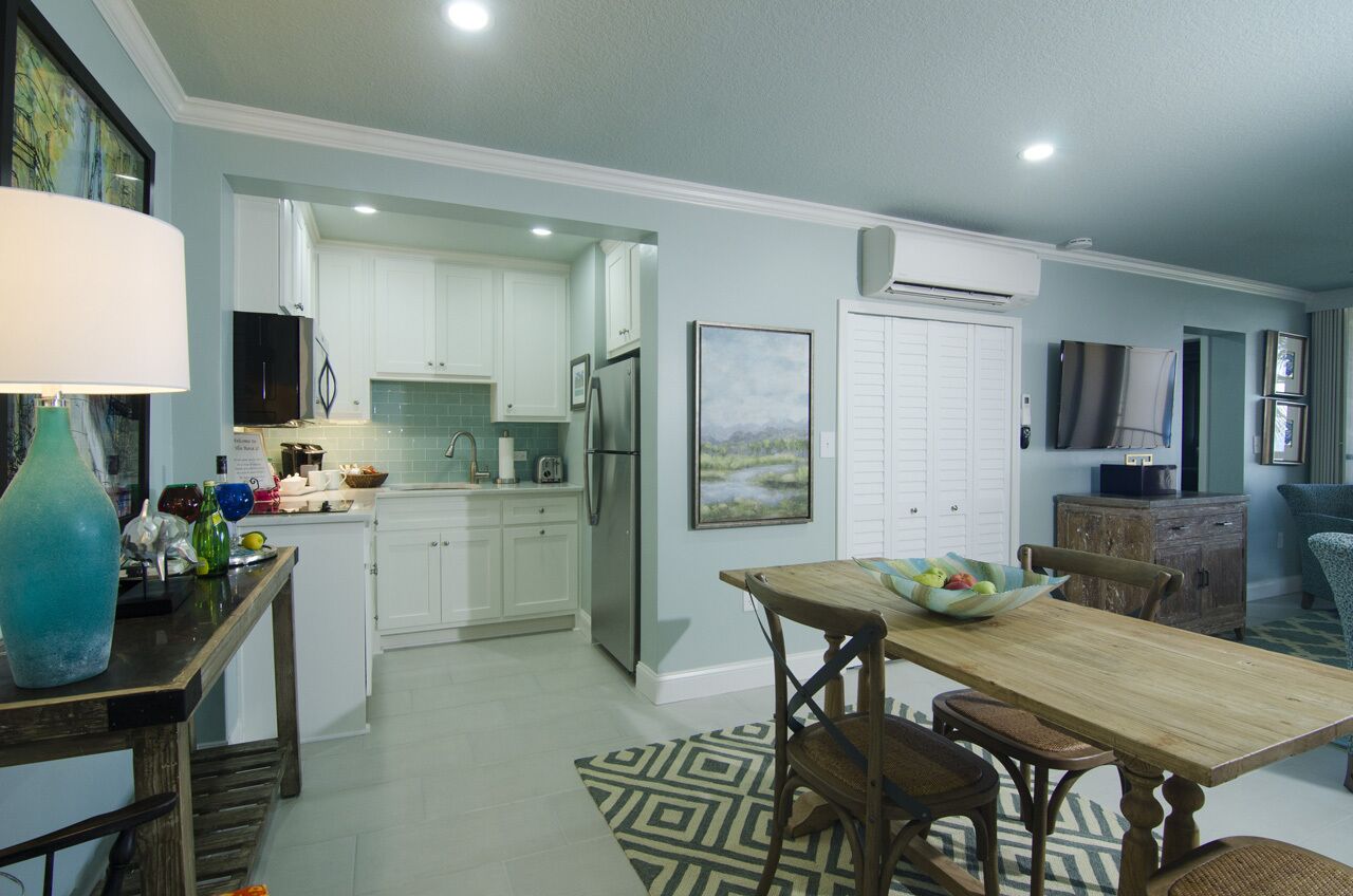 Una cocina moderna con armarios blancos, un refrigerador de acero inoxidable y un comedor con mesa y sillas de madera.