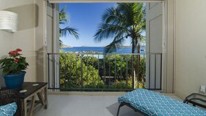 Un balcon avec vue sur la mer, des palmiers et un lit recouvert d’une couvre-lit à motifs.