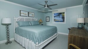 Une chambre à coucher avec un lit, un ventilateur de plafond, une fenêtre donnant sur un beau paysage et une commode en bois.
