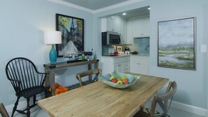 Un coin repas avec une table en bois, des chaises, un saladier de fruits, une lampe et des œuvres d’art accrochées aux murs.