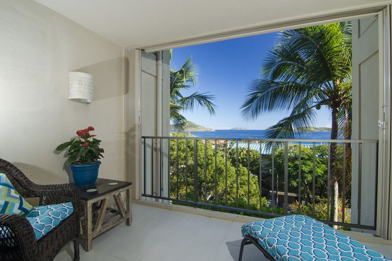 A balcony with a view of the sea, a wicker chair, a small table, and a potted plant.