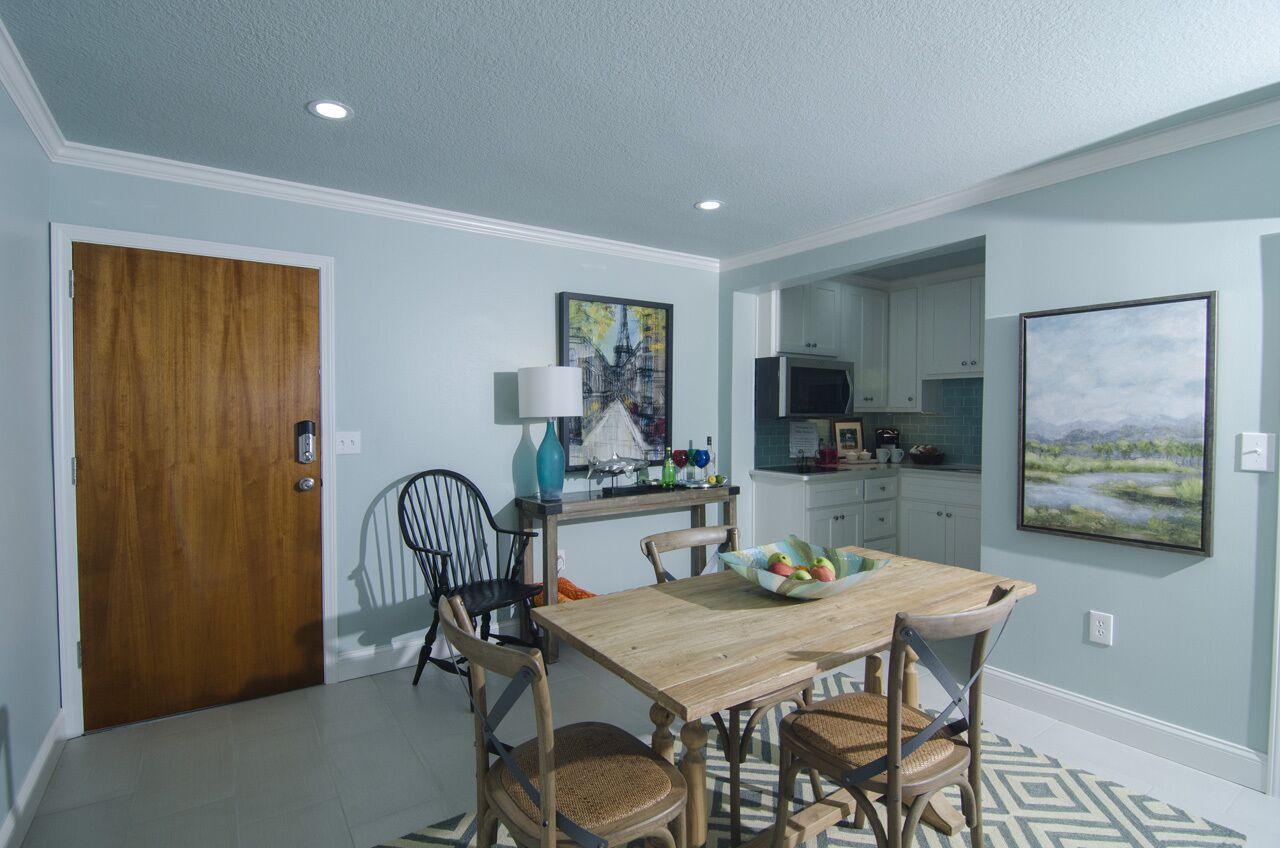 A dining area with a wooden table, four chairs, a vase, and a painting on the wall.