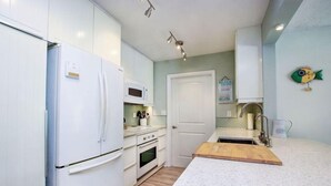 Eine moderne Küche mit weißen Schränken, einem weißen Kühlschrank, einer Mikrowelle, einer Holz Arbeitsplatte und einem Spülbecken.