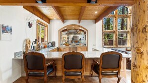 A wooden interior with a kitchen area, three chairs, and a large window. - Snow Summit Bike Ski Estate | Family Friendly (Big Bear Lake)