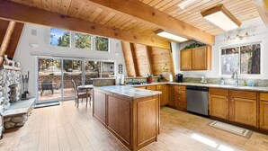 A spacious kitchen with wooden cabinets, a central island, and a large window overlooking a garden. - Snow Summit Bike Ski Estate | Family Friendly (Big Bear Lake)
