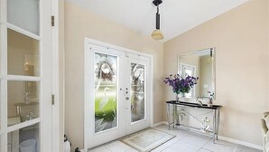 Une salle de bain avec un sol carrelé de carreaux blancs, une douche en verre, un meuble-lavabo avec un miroir et une plante en pot.