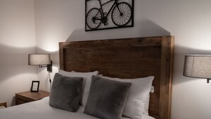 A neatly made bed with a wooden headboard, two bedside lamps, and a framed bicycle artwork above it.