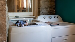 Un espace buanderie comprenant un lave-linge et un sèche-linge, une fenêtre avec des rideaux et un mur en pierre.