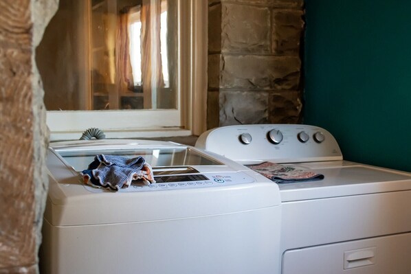 A laundry area with a washing machine and dryer, a window with curtains, and a stone wall.