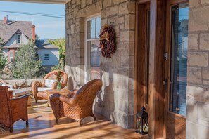A covered outdoor seating area with wicker furniture and a stone wall.