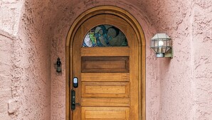 A wooden door with a glass panel, set in a pink stucco wall with a tiled entrance. - Western Moon - Private Retreat with Pool and Hot Tub (Tucson)