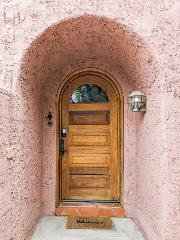 A wooden door with a glass panel, set in a pink stucco wall with a tiled entrance.