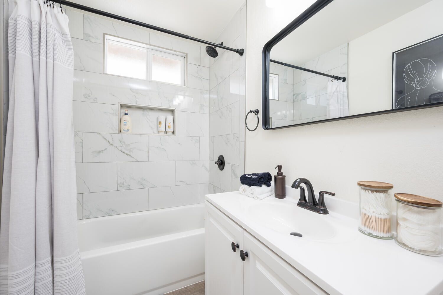 A modern bathroom with a white marble tile shower, a white vanity with a dark faucet, and a large mirror.