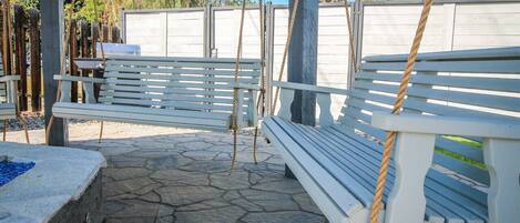 A stone-tiled outdoor area with white benches and ropes.