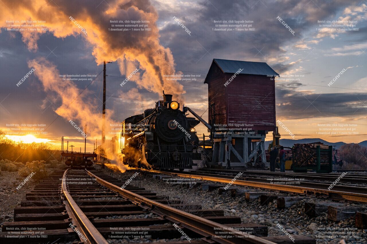 Uma locomotiva a vapor sobre trilhos de trem, com um armazém de carga ao fundo.