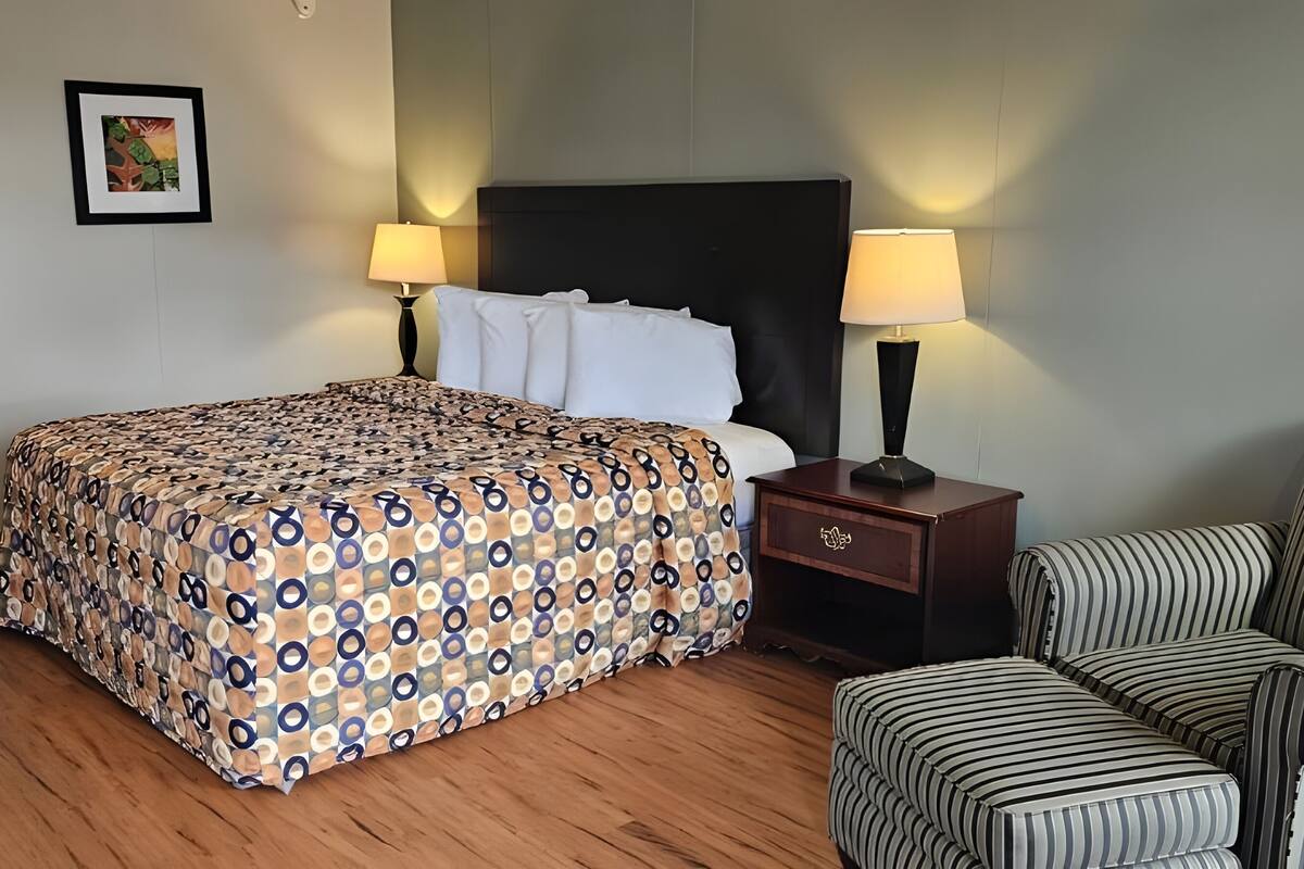 Una habitación de hotel con cama, dos lámparas de noche, un escritorio con silla y un sillón a rayas.
