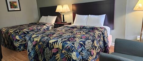 A hotel room with two beds, each with a floral bedspread, a nightstand with a lamp, and a framed picture on the wall.