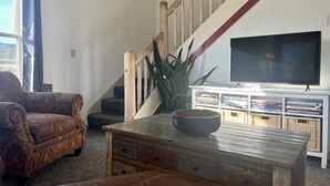 Un soggiorno con un divano, un tavolino da caffè con una ciotola, una TV su un mobile e una scala con ringhiere in legno.