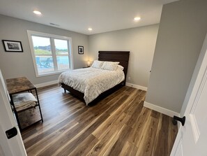 Ein Schlafzimmer mit einem großen Bett, einem kleinen Tisch, einem Sessel und einem Fenster mit Blick ins Freie.