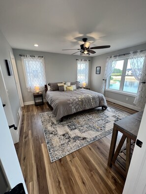 Relax in this serene bedroom with a large bed, bedside tables, and a ceiling fan, offering a view of the outdoors through large windows.