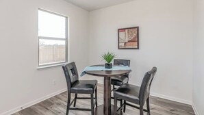 Un comedor con una mesa redonda, cuatro sillas, una planta en maceta y un cuadro en la pared.
