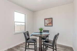 Un comedor con una mesa redonda, cuatro sillas, una planta en maceta y un cuadro en la pared.