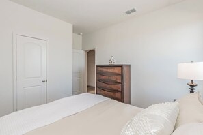 A bedroom with a bed, a wooden shelf unit, and a lamp. - Amazing Contemporary 4BR New Retreat ~ Fam&Group (Seagoville)