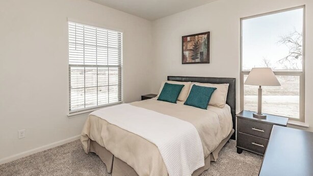Un dormitorio con cama, mesita de noche, lámpara y ventana.