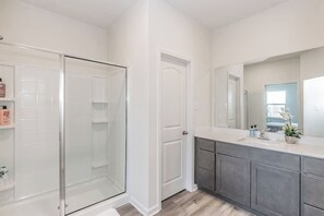 Un baño moderno con cabina de ducha de vidrio, un espejo grande y un mueble de tocador de tonos oscuros.