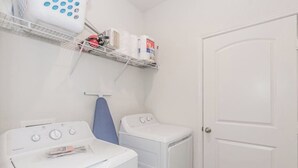 Un área de lavandería con dos lavadoras blancas, un tendedero y estantes con productos de limpieza.