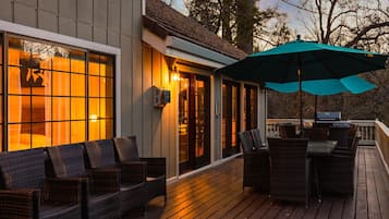 A wooden deck with wicker furniture and a grill, overlooking a forested area.