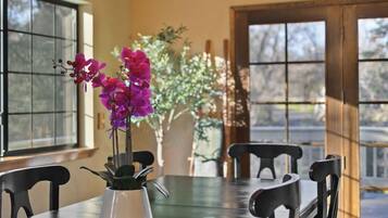 A dining area with a wooden ceiling, a chandelier, a table with chairs, and a vase with purple flowers.