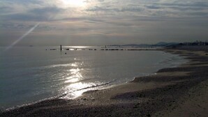 Une plage aux eaux calmes, une jetée qui se dessine à l’horizon et un ciel nuageux.