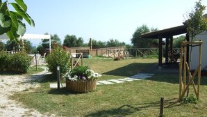 Un espace extérieur abrité, doté d’une pergola en bois, d’un coin salon avec des chaises et d’un chemin menant à un bâtiment.