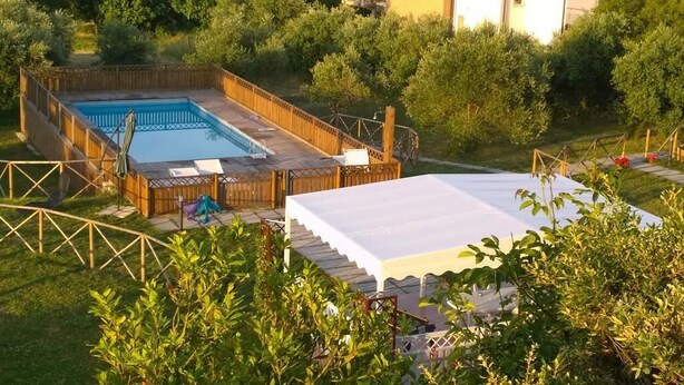 Un jardin avec une piscine, une terrasse en bois et un espace salon abrité.