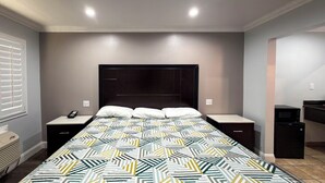 Ein Schlafzimmer mit einem Bett, Nachttischen, einem Heizgerät, einer Mikrowelle und einem Fenster mit Jalousien.