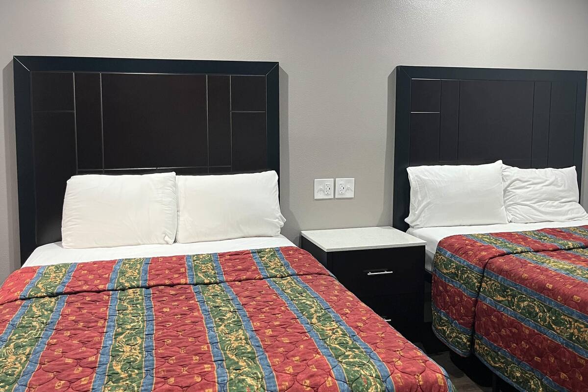 Een hotelkamer met twee bedden, elk met een zwart hoofdeinde, witte beddengoed en een deken met een rood en groen patroon. Tussen de bedden staat een klein, zwart nachtkastje.