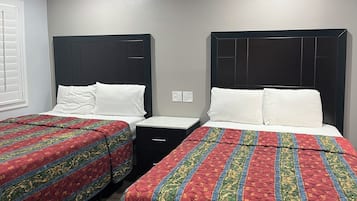 Deux lits jumeaux identiques, avec des têtes de lit et des pieds de lit assortis, chacun agrémenté d’un oreiller blanc et d’une couverture colorée. Une petite table de chevet avec un tiroir se trouve entre les deux lits.