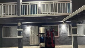 Ein Coca-Cola Getränkeautomat vor einem Gebäude mit einem belebten Eingangstor und einem Balkon.