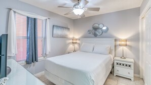 Ein Schlafzimmer mit einem Bett, Nachttischen, einem Deckenventilator und einem Fenster mit Vorhängen.