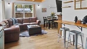 A cozy living room with a brown leather sofa, a wooden dining table, and a bar area with stools.
